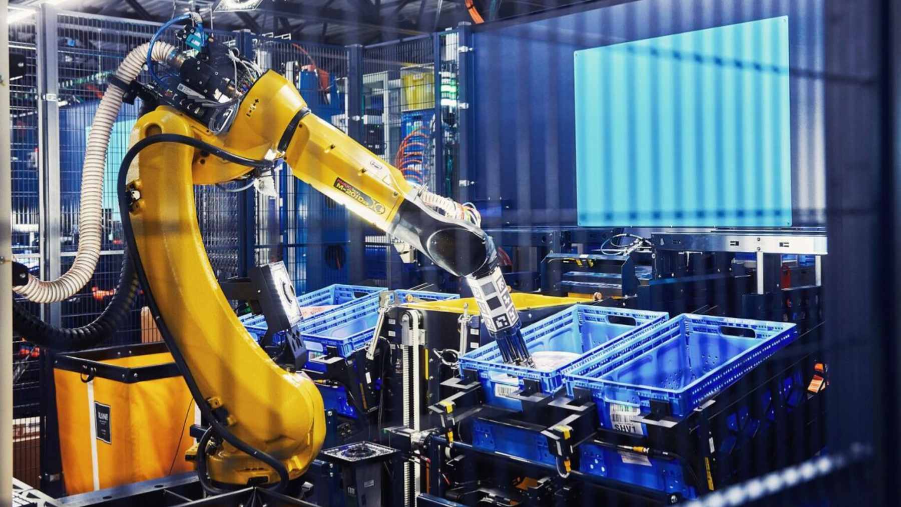 An automated Amazon "Proteus" mobile robot navigating a fulfillment center floor near stacked yellow storage bins.