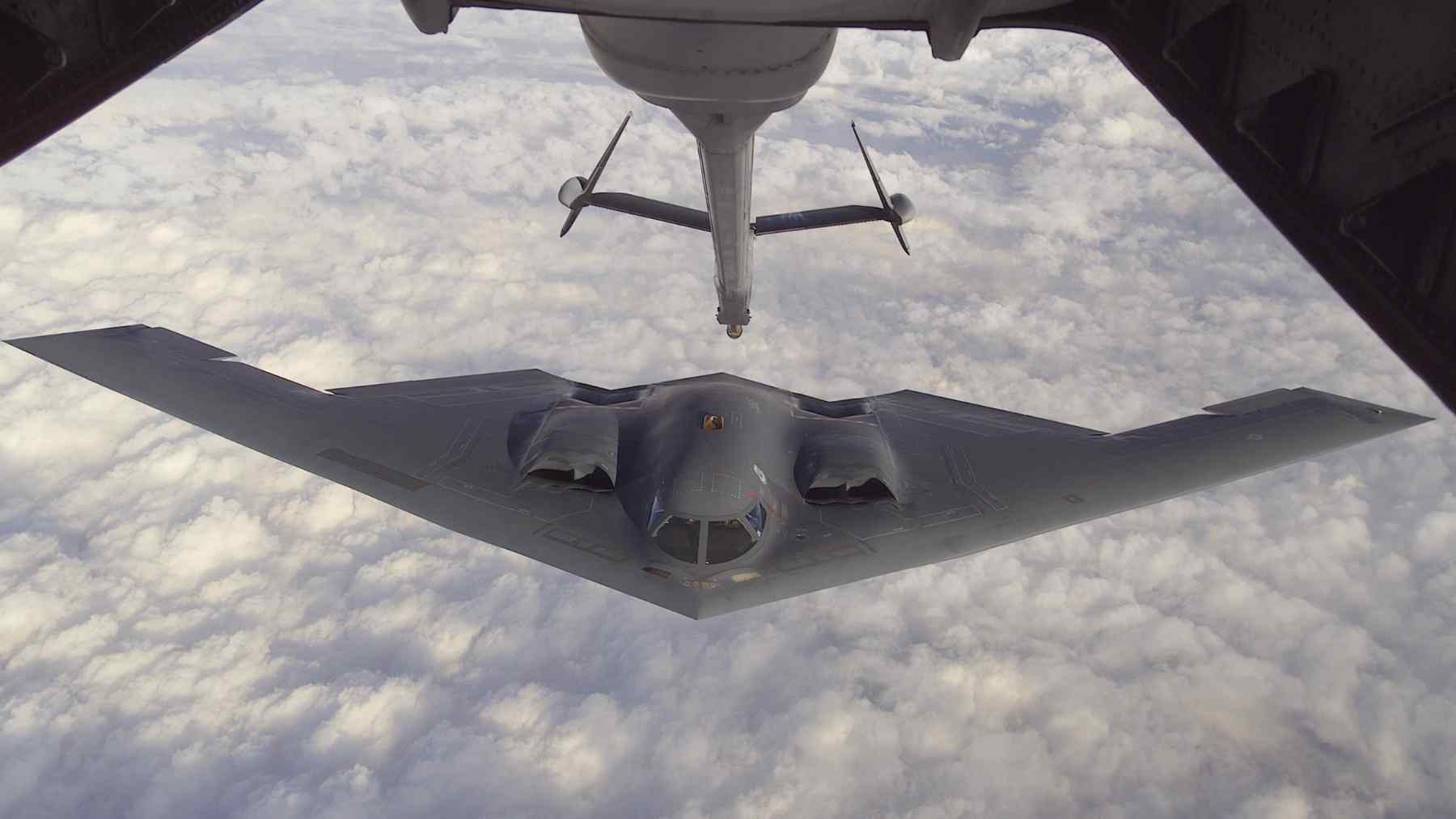 U.S. Air Force B-2 Spirit stealth bomber receives fuel from a tanker during aerial refueling above a cloud deck.