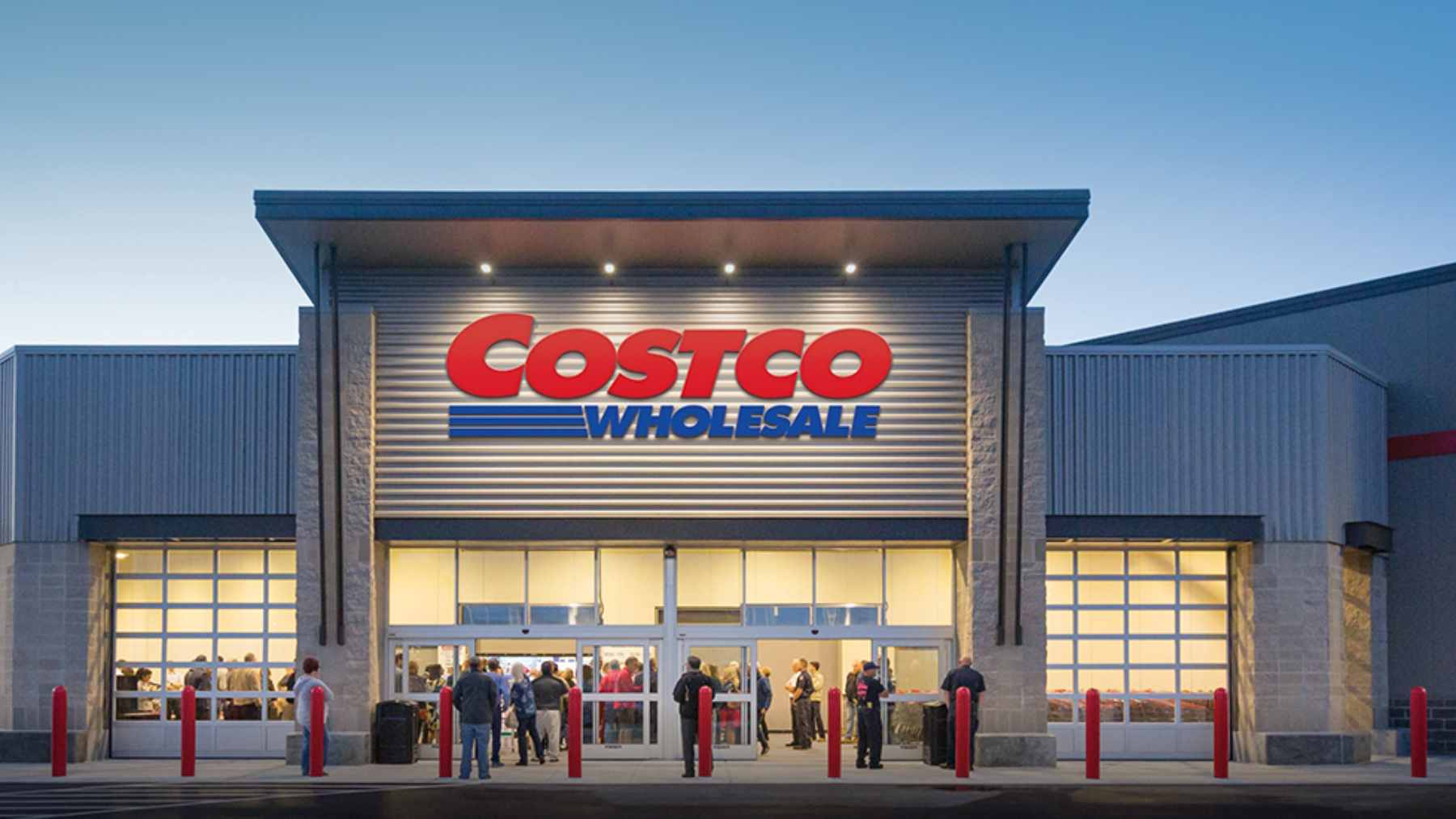 A Costco customer service desk where an employee is carefully reviewing a member's return receipt alongside a shopping cart of merchandise.