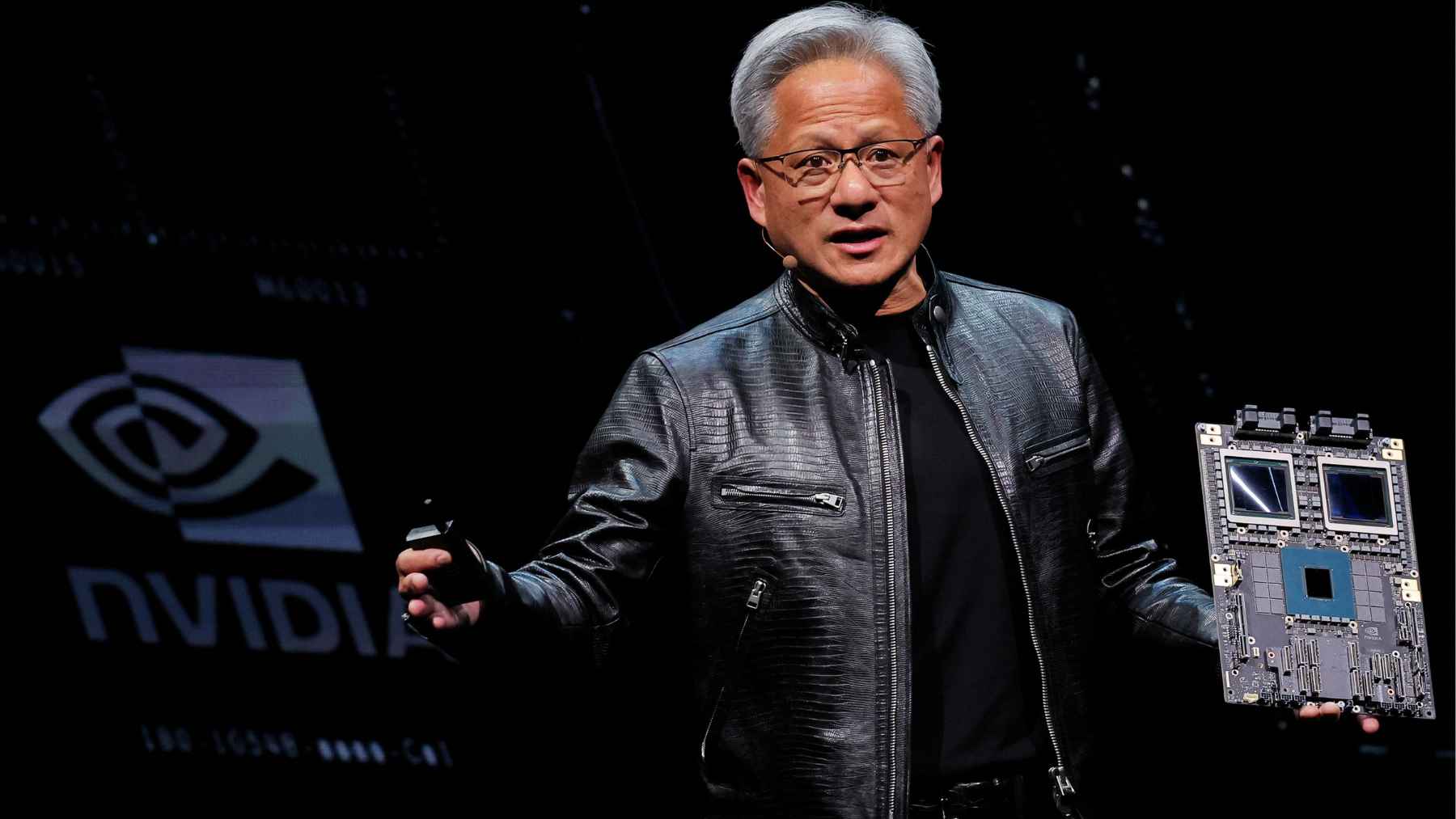 Nvidia is reviving production of a key AI chip variant for China, and the move exposes just how complicated the global tech war has become 1 Jensen Huang speaking onstage while holding an Nvidia AI chip board, illustrating the company’s renewed China-compliant chip production