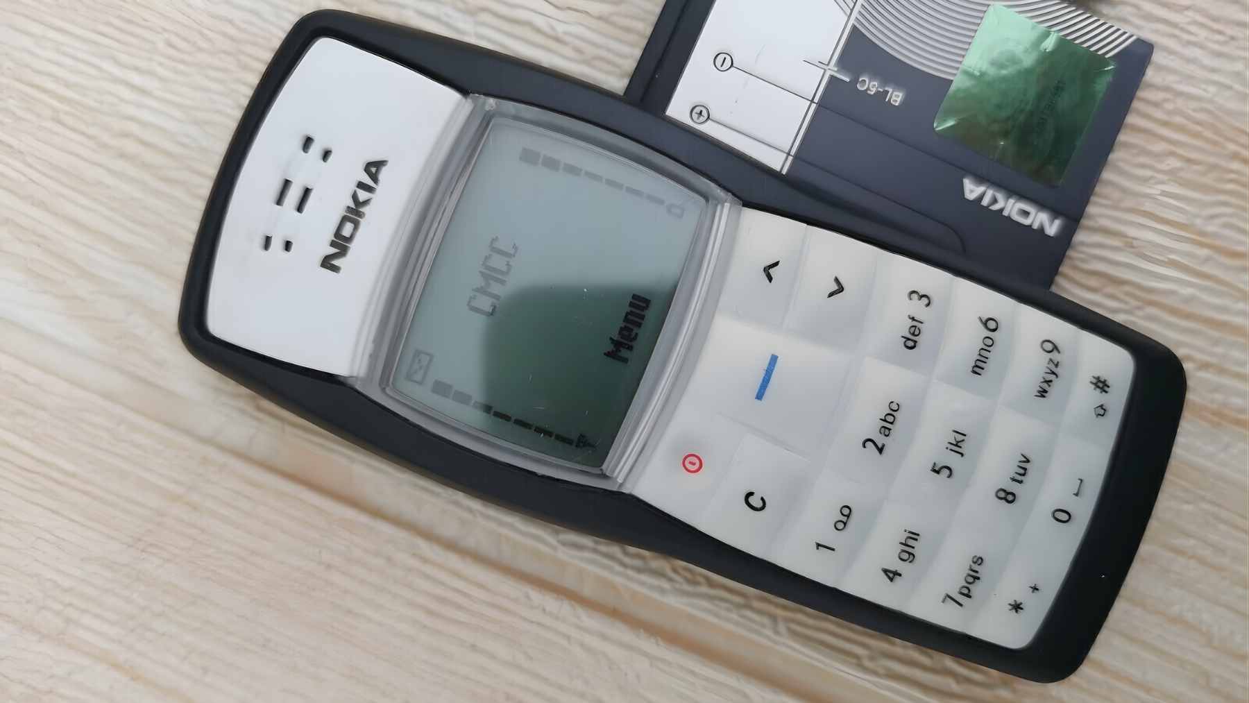 A classic silver Nokia 1100 mobile phone with its iconic monochrome screen and rubberized keypad.