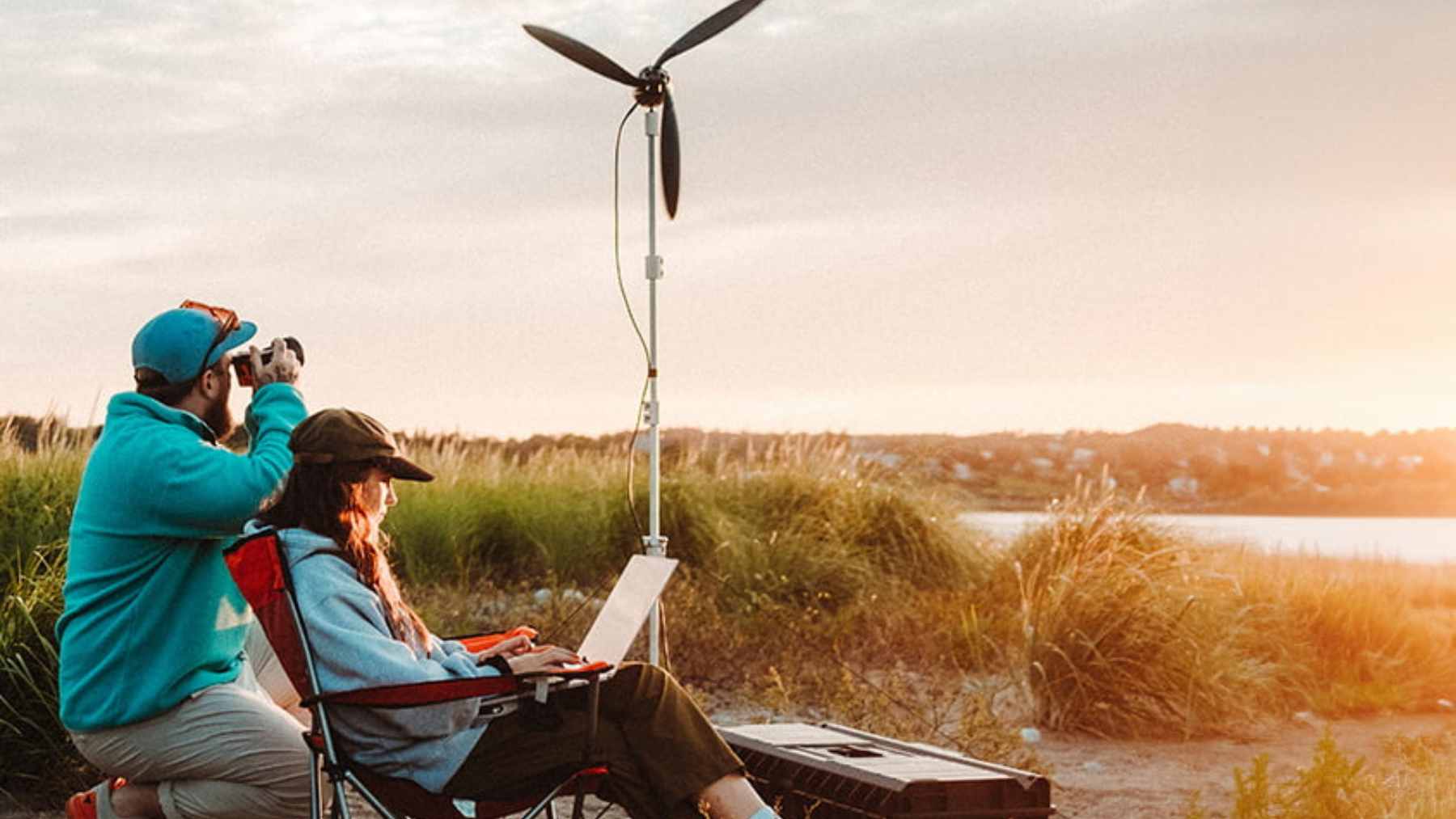 The Shine 2.0 portable wind turbine deployed on its ground mount in a coastal setting, with its three blades spinning to generate power.