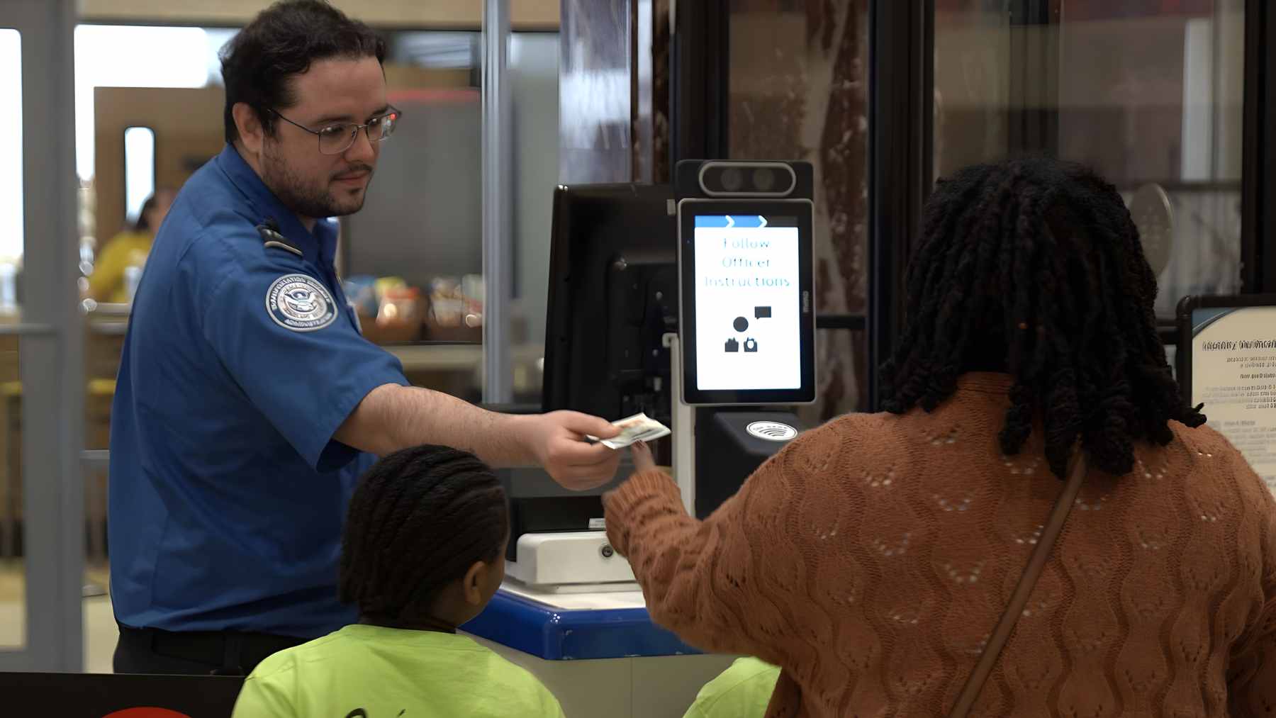 A passenger at a TSA airport security checkpoint holding a smartphone showing a $45 ConfirmID payment receipt.