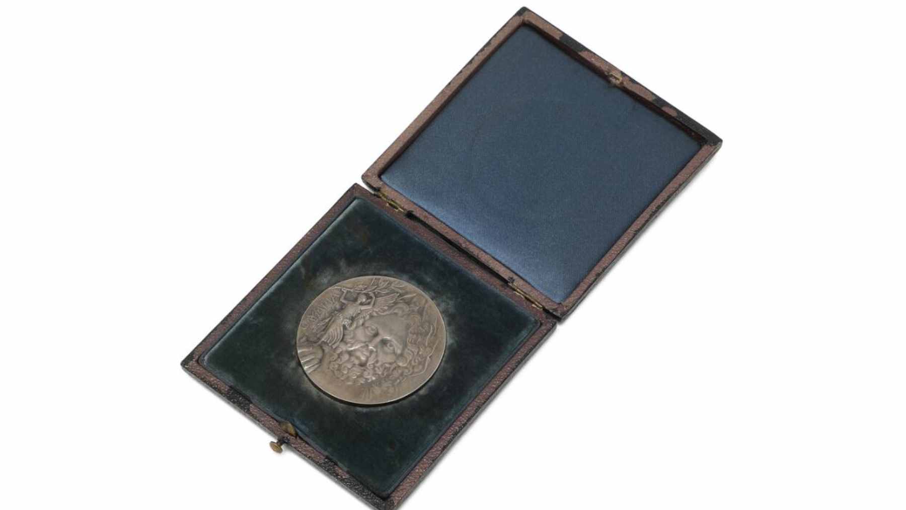 A close-up view of the 1896 Athens Olympic silver medal featuring the engraved image of Zeus and Nike.
