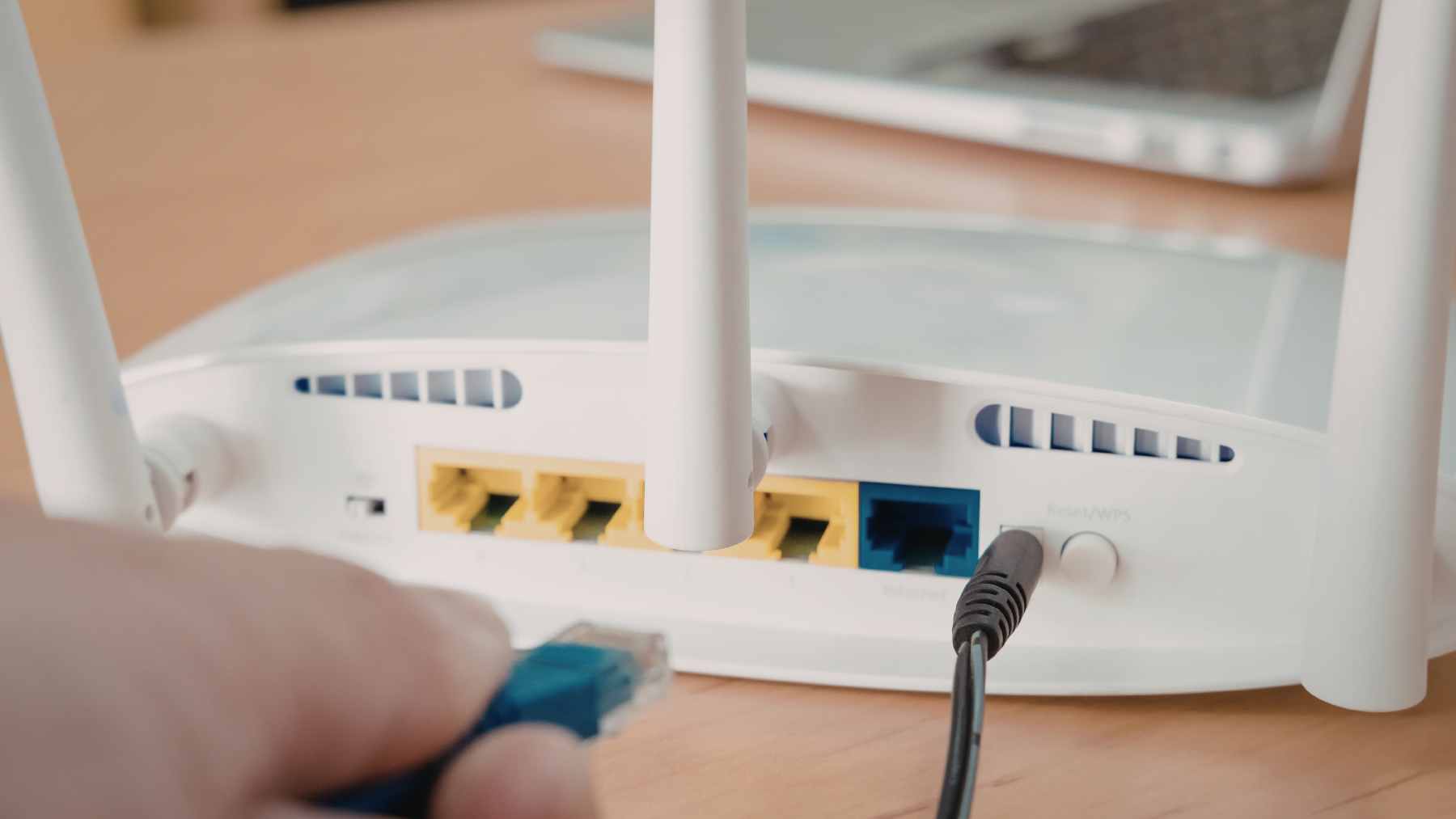 A close-up shot of a modern home Wi-Fi router with glowing indicator lights sitting on a wooden desk.