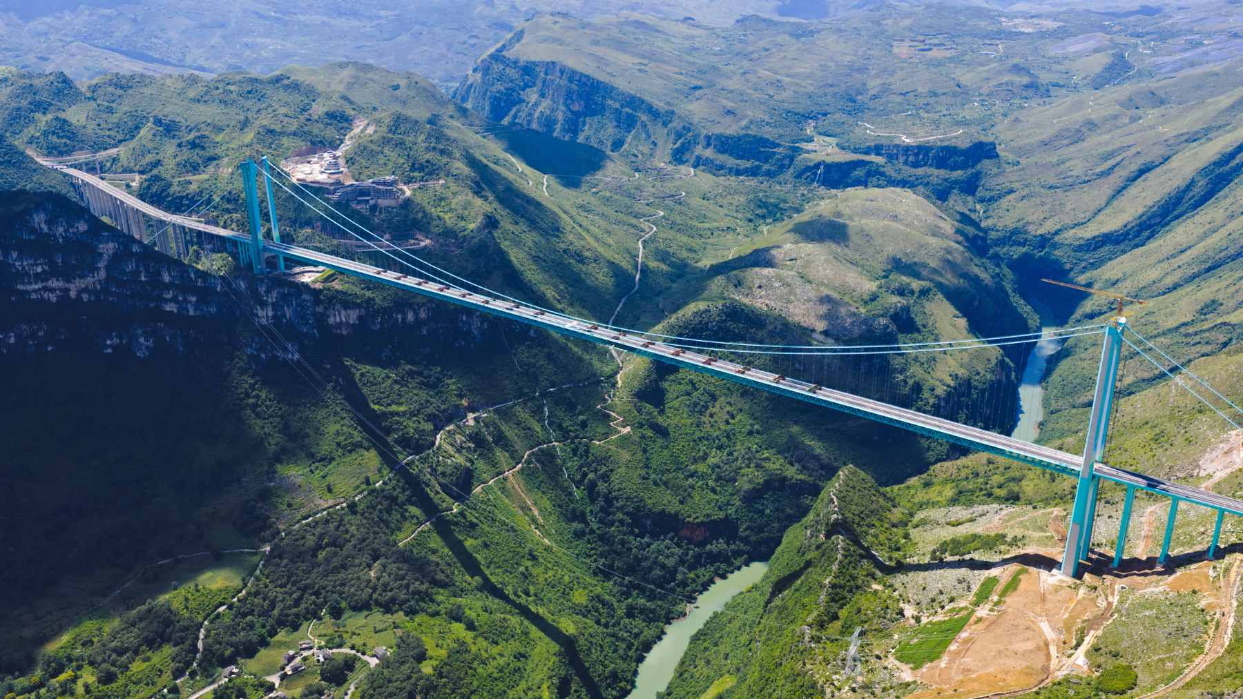 A massive suspension bridge spanning a deep, misty canyon, featuring an artificial waterfall cascading from its structure.