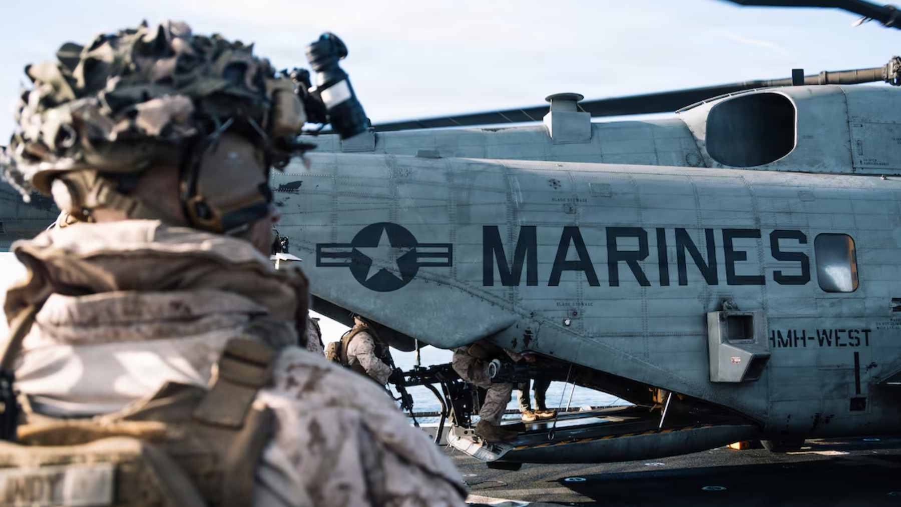 A group of heavily equipped U.S. Marines conducting a search operation in a dense, rain-soaked forest environment.