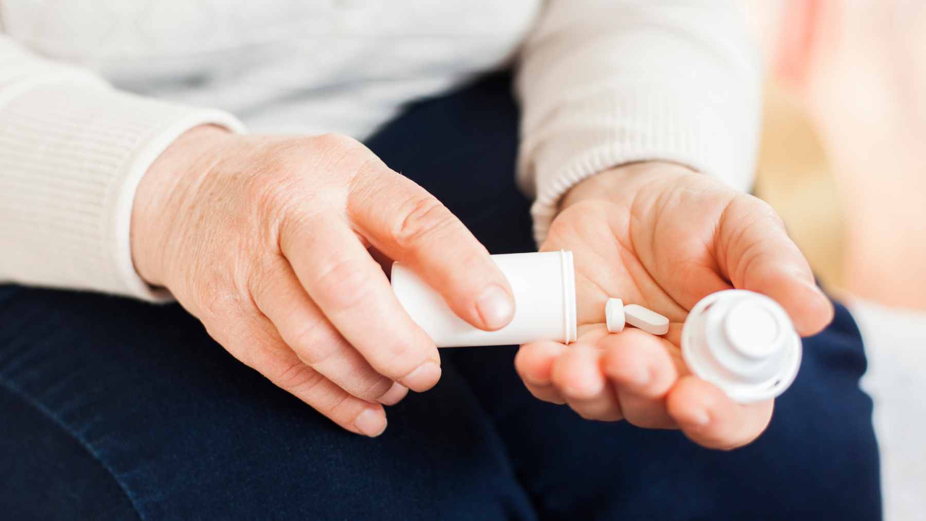A close-up view of a pharmacist's hand counting prescription pills on a tray next to an open pill bottle.