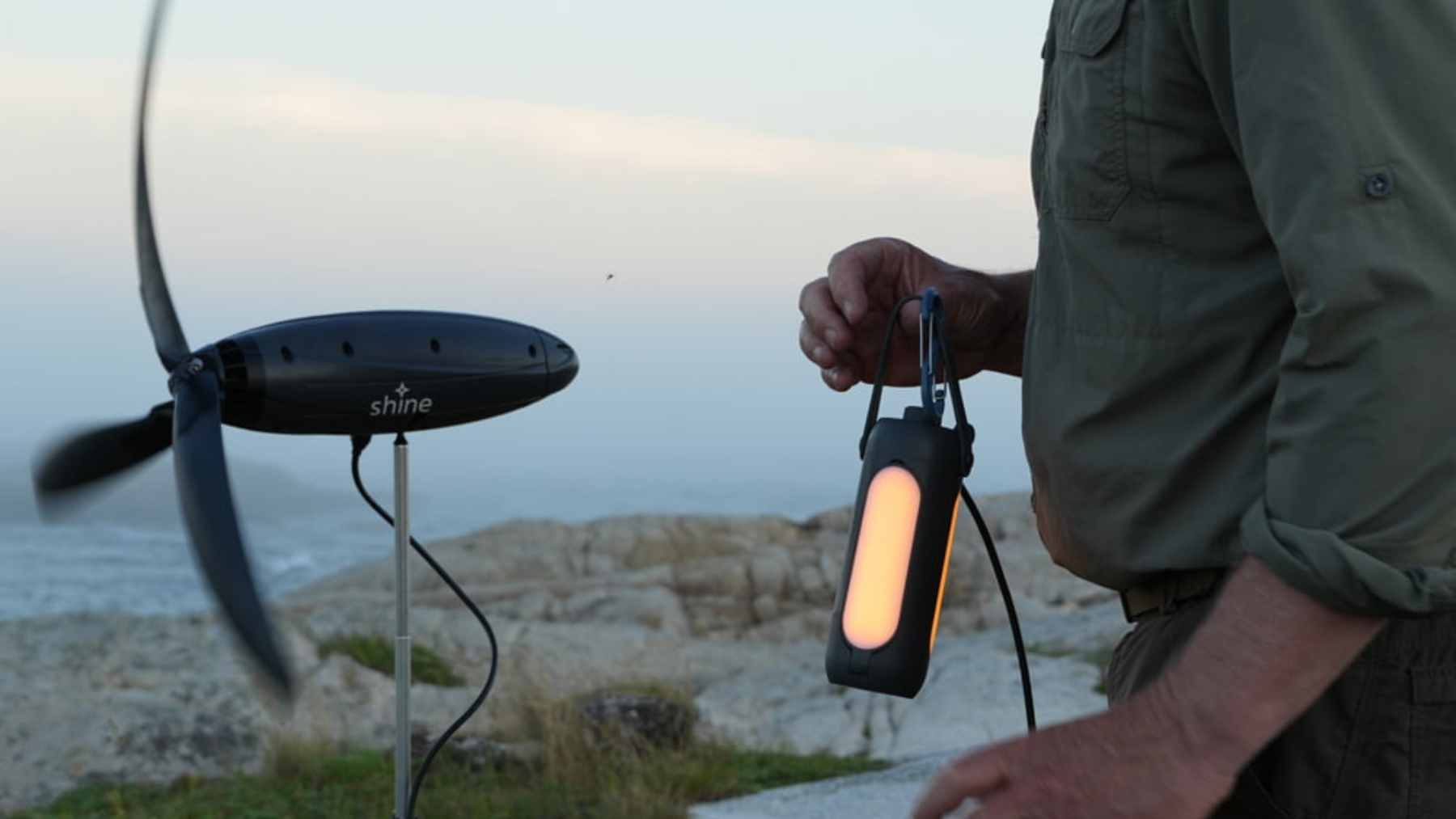 A compact, portable Shine 2.0 wind turbine set up on a tripod in a grassy outdoor landscape.