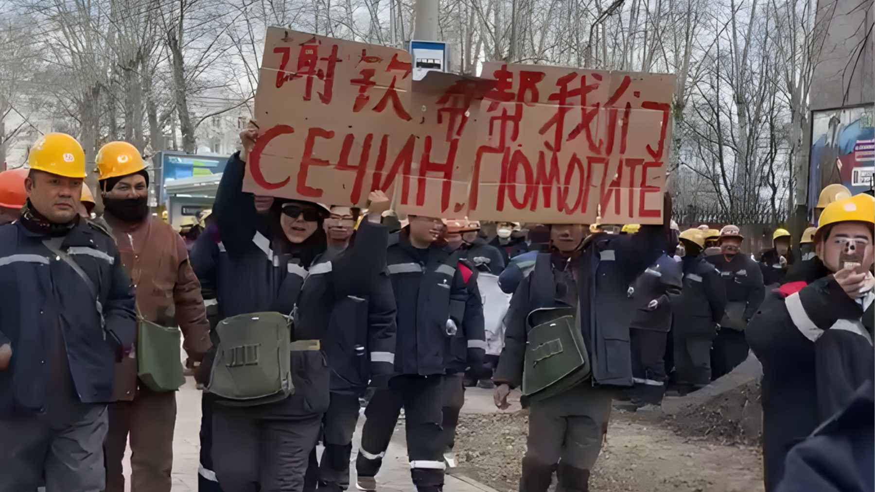 A large crowd of Chinese workers protesting with signs on a street near an industrial refinery site in Russia.