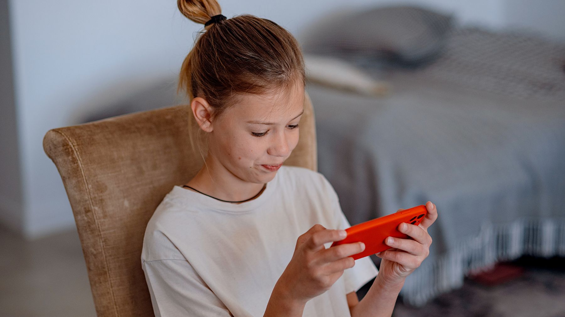 Niña usando el móvil en su habitación, ejemplo del aumento de adicción digital en menores.