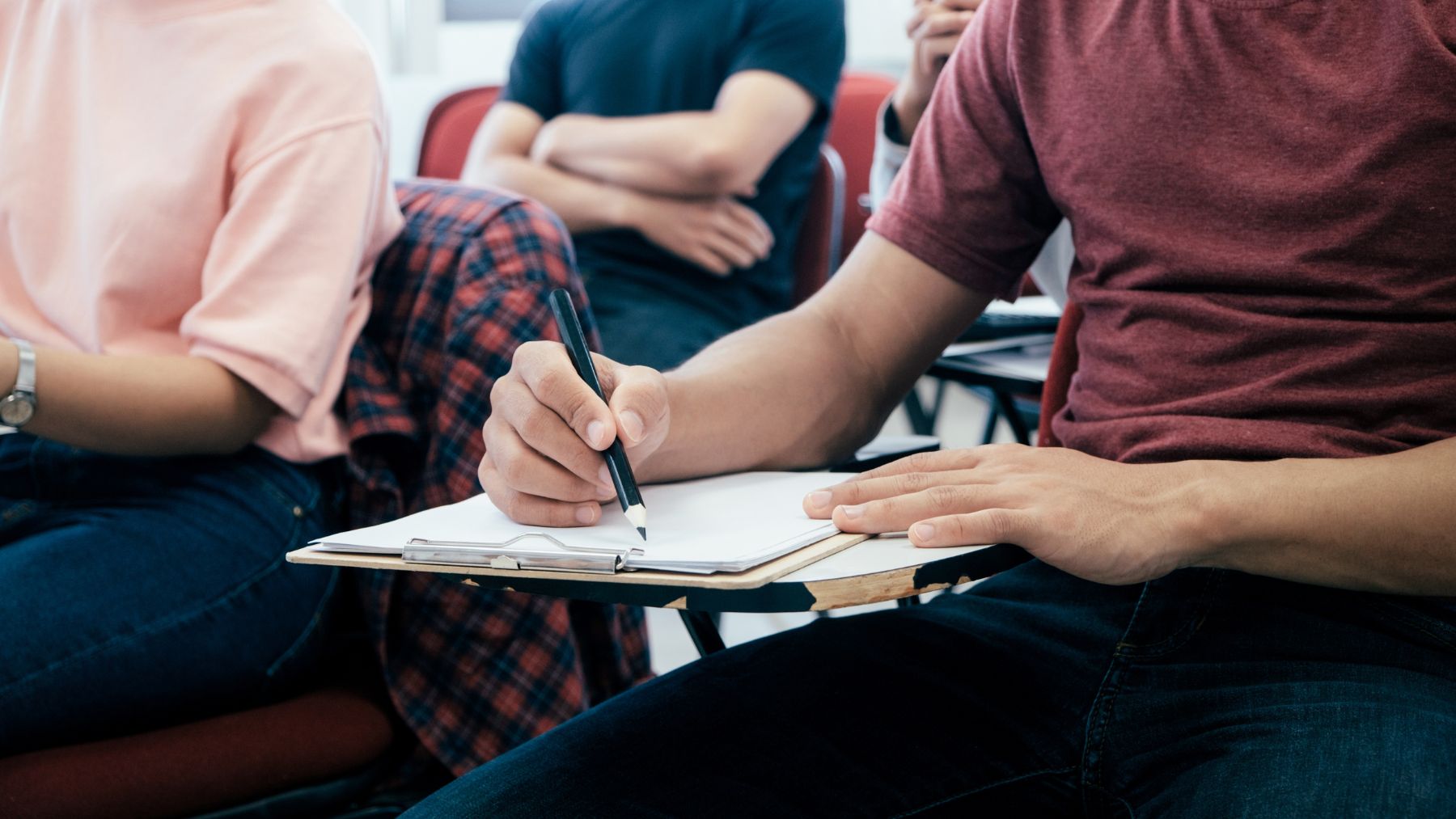 Estudiantes universitarios en clase escribiendo apuntes en un aula durante un examen.